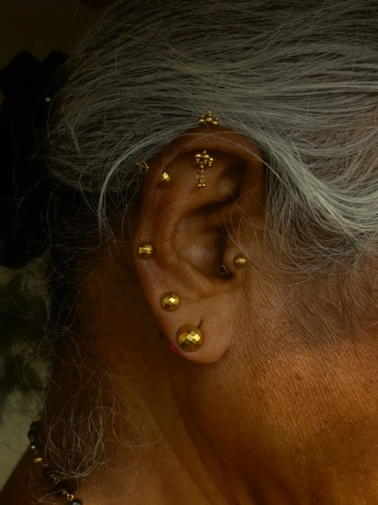 Oreille portant plusieurs piercings à bijoux dorés, du lobe à l'hélix