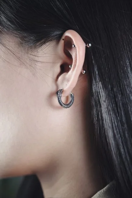 Gros plan d'une oreille : anneau au lobe et deux piercings d'hélix.