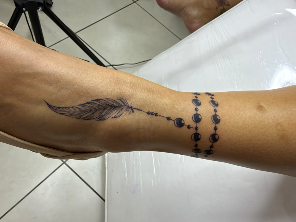 Plume et chapelet au poignet — tatouage réalisé au studio AUREA Lab, Antananarivo